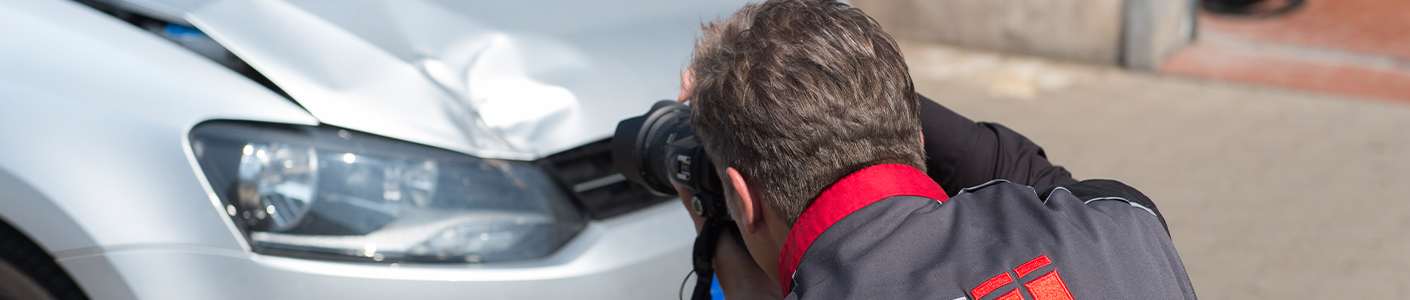 Gutachter fotografiert Frontschaden an einem silberfarbenem Auto